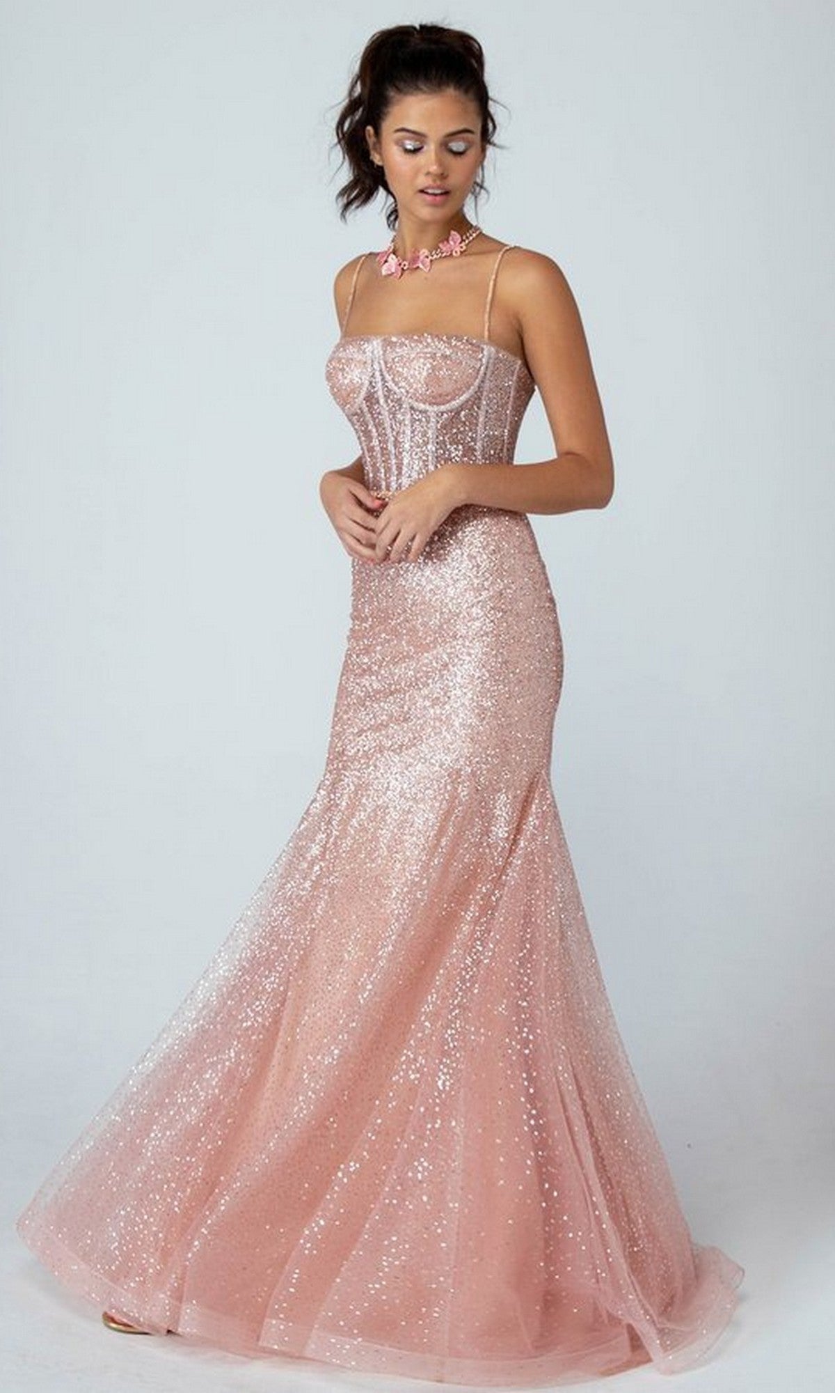 A woman stands against a plain background wearing the Eureka 9911 Long Prom Dress in rose gold, featuring thin straps, sparkling glitter fabric, a fitted corset bodice, and a flared tulle skirt.